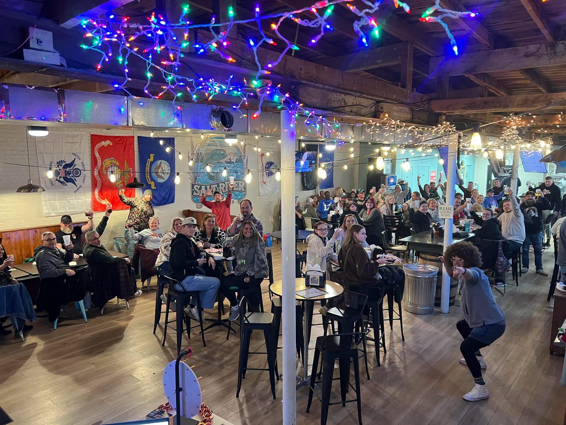 A full taproom raising their glasses under string lights at Salt River Brewing