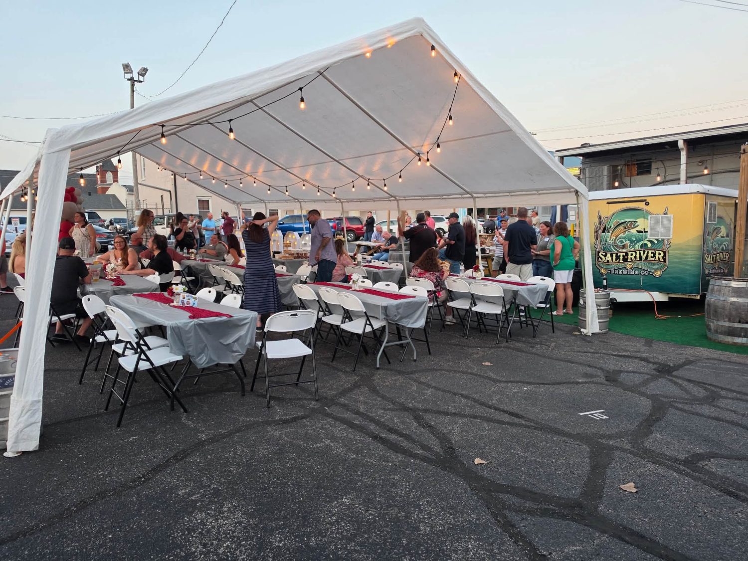 Guests at long tables under a lit tent next to the Salt River beer trailer